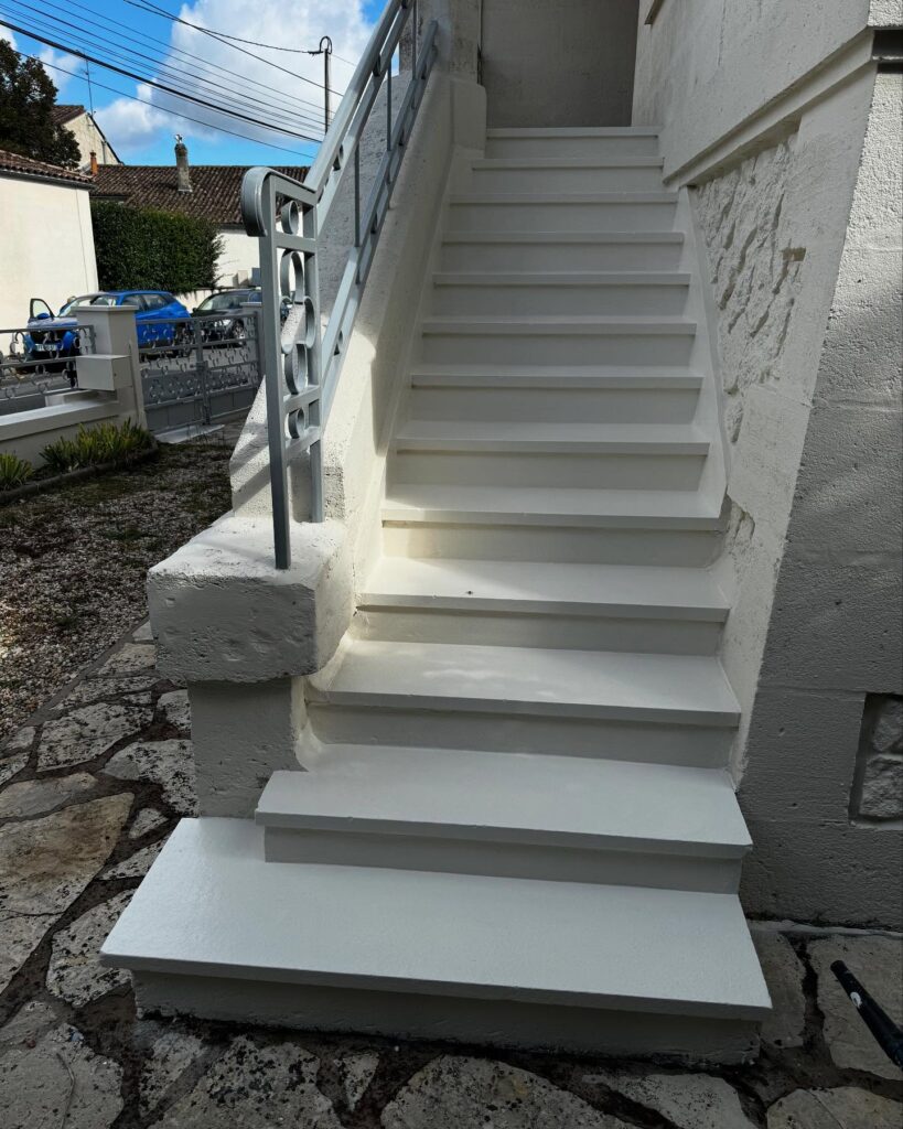 Escalier extérieur blanc : rénovation, marches et rampe moderne. Escalier extérieur rénové, marches blanches et rampe métallique grise décorative. Façade immaculée et dalles de pierre sous un ciel bleu.