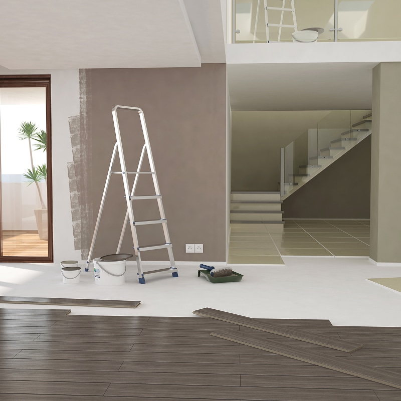 Pose parquet et peinture : Rénovation moderne du salon Rénovation intérieure : pose de parquet stratifié et peinture murale taupe avec échelle, pots de peinture et rouleau dans un espace moderne.